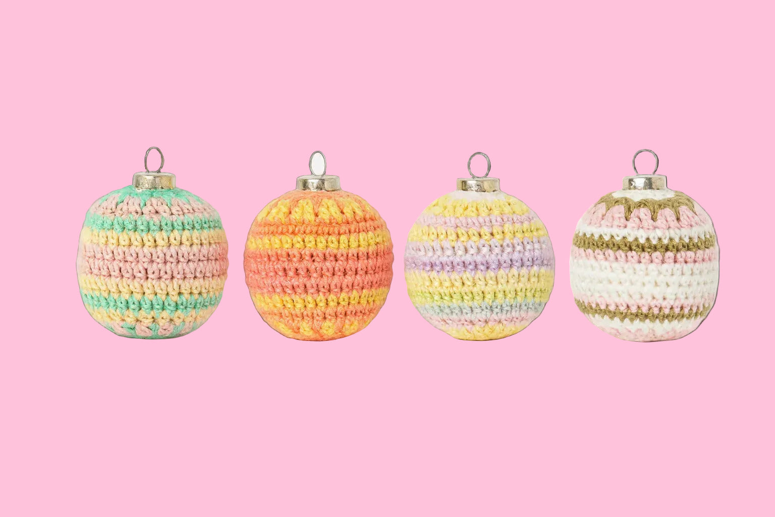 Four crocheted Christmas balls in pastel colors on a pink background